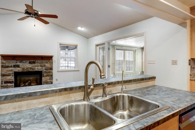 kitchen with lofted ceiling, sink, a wealth of natural light, and a stone fireplace