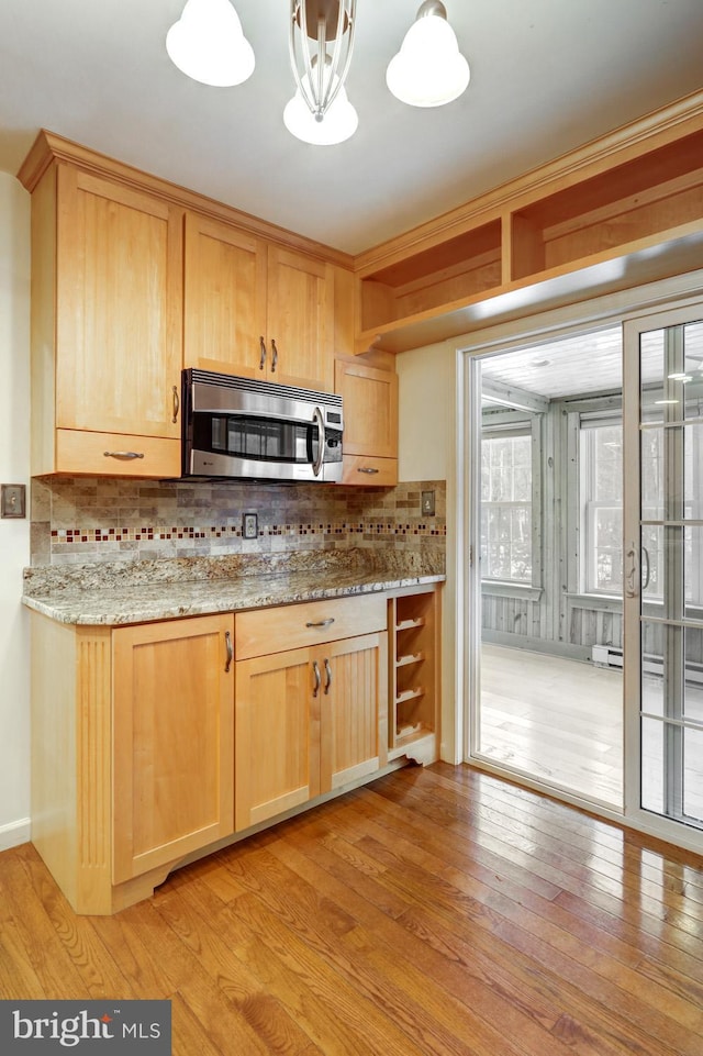 kitchen with light brown cabinetry, decorative light fixtures, light hardwood / wood-style flooring, light stone countertops, and decorative backsplash