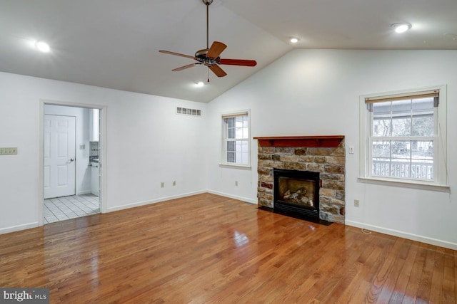 unfurnished living room with ceiling fan, a stone fireplace, lofted ceiling, and light wood-type flooring