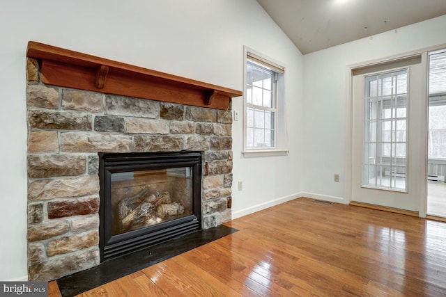 unfurnished living room with hardwood / wood-style flooring, vaulted ceiling, and a stone fireplace