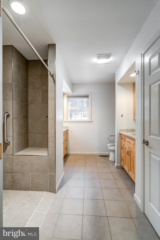 bathroom with tile patterned flooring, vanity, tiled shower, and toilet