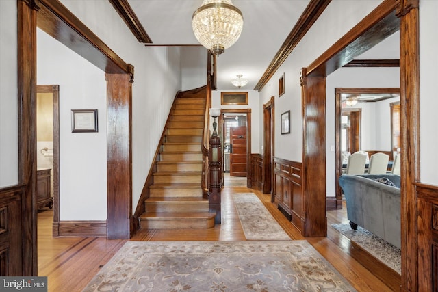 foyer entrance with crown molding, a notable chandelier, and light wood-type flooring