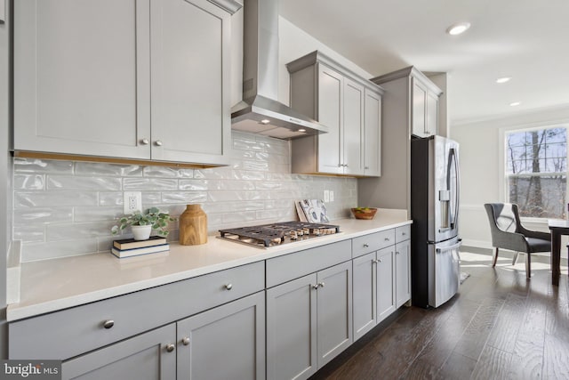 kitchen featuring appliances with stainless steel finishes, gray cabinetry, decorative backsplash, dark wood-type flooring, and wall chimney exhaust hood