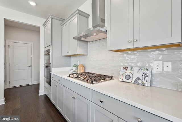 kitchen featuring gray cabinets, backsplash, stainless steel appliances, dark wood-type flooring, and wall chimney exhaust hood