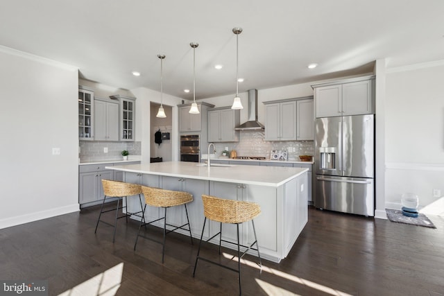 kitchen featuring pendant lighting, wall chimney range hood, gray cabinetry, stainless steel appliances, and an island with sink