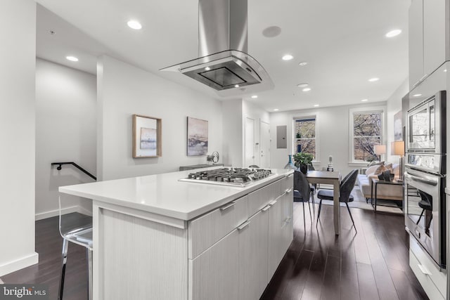 kitchen with appliances with stainless steel finishes, a breakfast bar area, island exhaust hood, a center island, and dark wood-type flooring