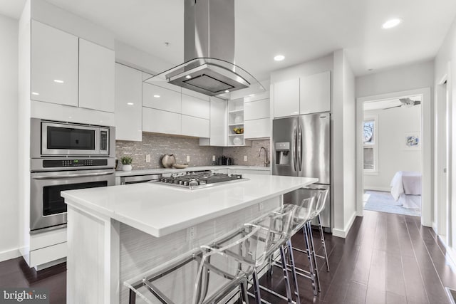 kitchen with a kitchen island, island range hood, a breakfast bar area, white cabinets, and stainless steel appliances