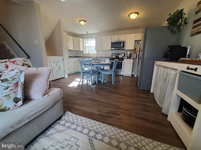 kitchen featuring sink, appliances with stainless steel finishes, dark hardwood / wood-style floors, white cabinets, and decorative light fixtures