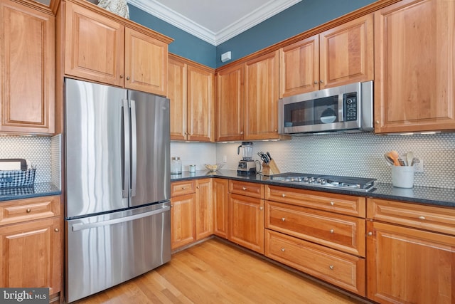 kitchen featuring dark stone countertops, stainless steel appliances, tasteful backsplash, ornamental molding, and light hardwood / wood-style floors