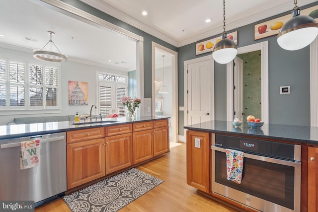 kitchen with appliances with stainless steel finishes, sink, hanging light fixtures, ornamental molding, and light hardwood / wood-style flooring