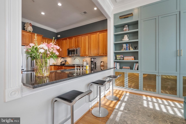 kitchen featuring sink, crown molding, dark stone countertops, kitchen peninsula, and stainless steel appliances