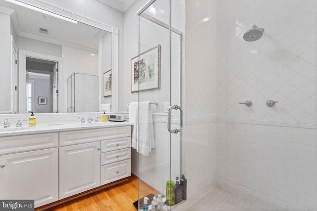 bathroom with a shower with door, crown molding, hardwood / wood-style floors, and vanity