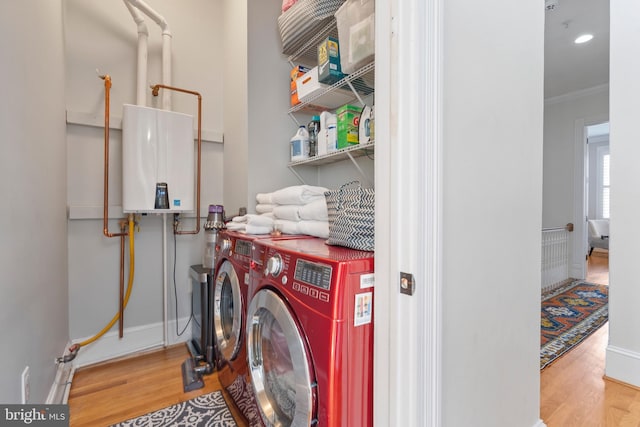 washroom featuring ornamental molding, light hardwood / wood-style flooring, washing machine and dryer, and tankless water heater