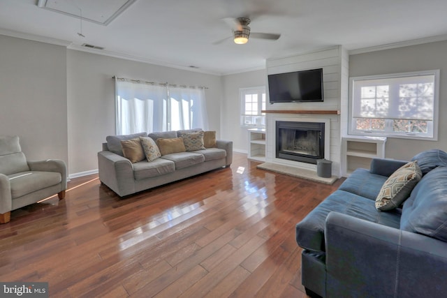 living room with hardwood / wood-style floors, ornamental molding, a large fireplace, and ceiling fan