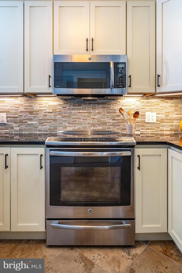 kitchen featuring white cabinetry, decorative backsplash, stainless steel appliances, and dark stone countertops