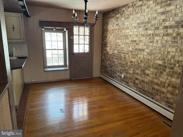 unfurnished dining area with a notable chandelier, a baseboard radiator, wood-type flooring, and brick wall