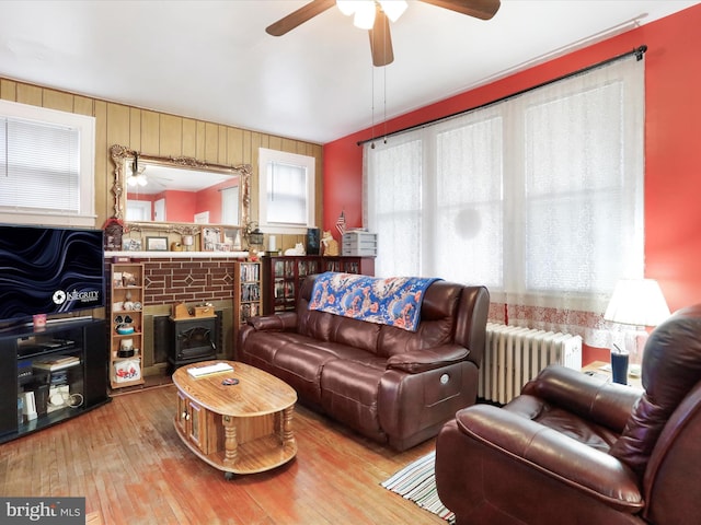 living room featuring ceiling fan, radiator heating unit, light wood-type flooring, and a wood stove