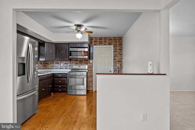 kitchen featuring dark brown cabinetry, appliances with stainless steel finishes, ceiling fan, brick wall, and backsplash