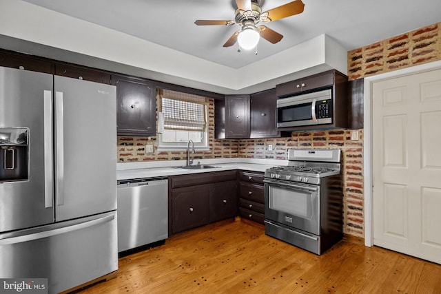 kitchen featuring sink, dark brown cabinets, stainless steel appliances, brick wall, and light wood-type flooring