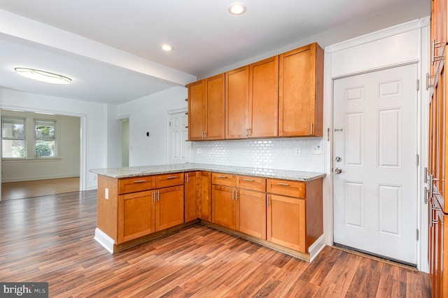 kitchen featuring tasteful backsplash, light stone countertops, hardwood / wood-style floors, and kitchen peninsula