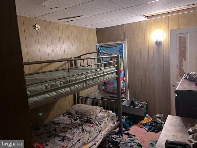 carpeted bedroom featuring a drop ceiling and wood walls