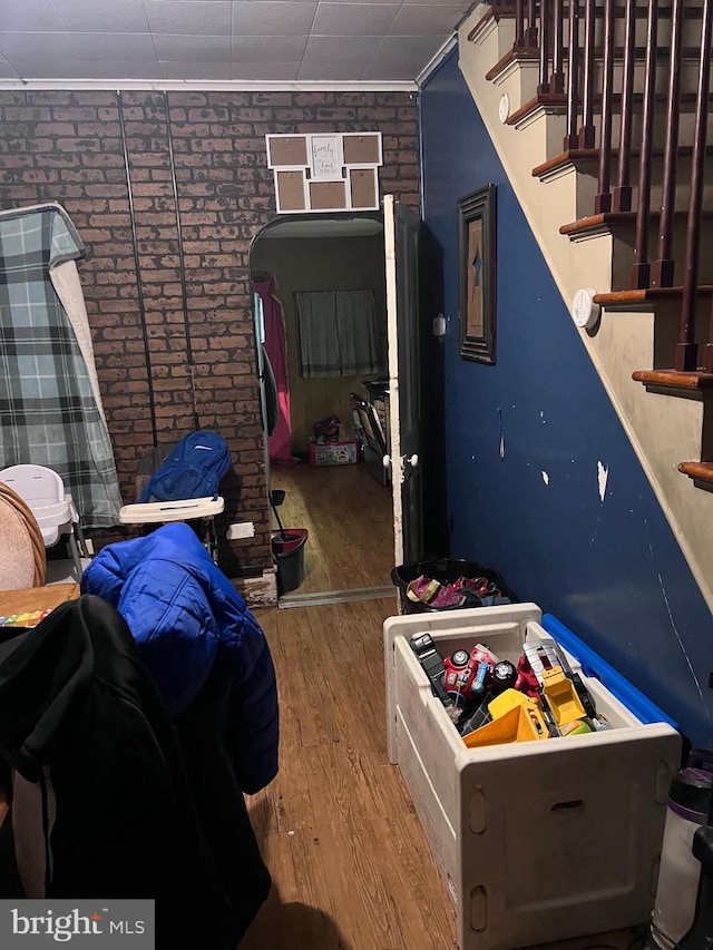 bedroom featuring ornamental molding, brick wall, and wood-type flooring