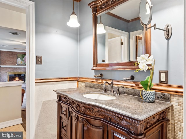 bathroom with crown molding, vanity, and a brick fireplace