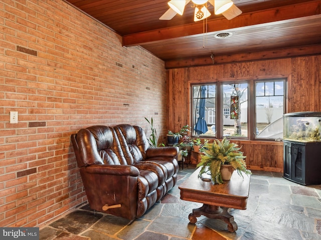 living room featuring beamed ceiling, ceiling fan, brick wall, and wooden ceiling