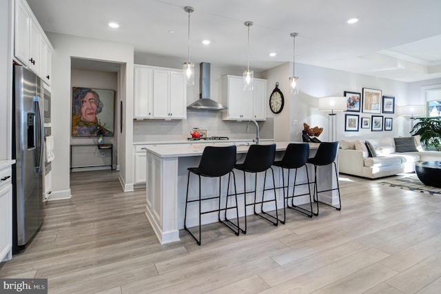 kitchen featuring wall chimney exhaust hood, a breakfast bar area, appliances with stainless steel finishes, open floor plan, and light countertops