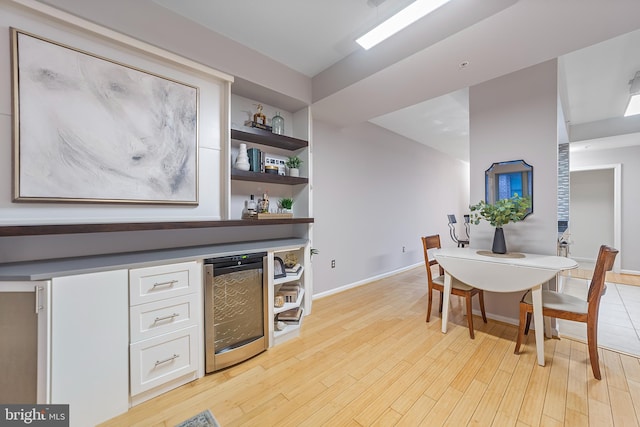 dining room featuring wine cooler, built in shelves, light hardwood / wood-style floors, and bar area