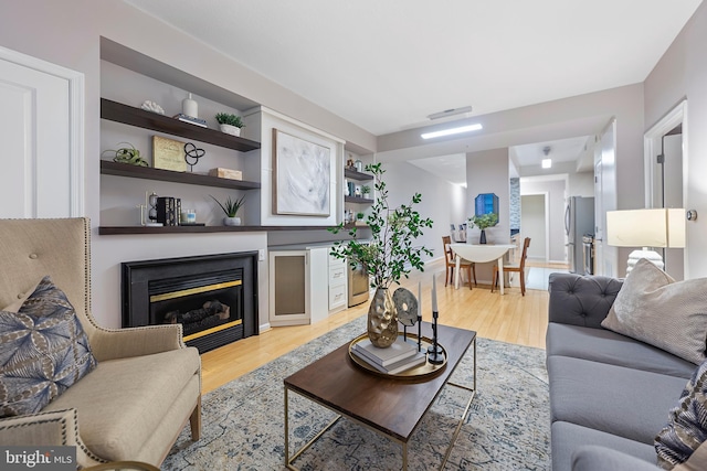 living room with built in shelves and light hardwood / wood-style flooring