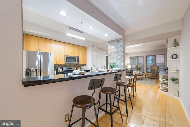 kitchen with a kitchen bar, sink, light wood-type flooring, kitchen peninsula, and stainless steel appliances