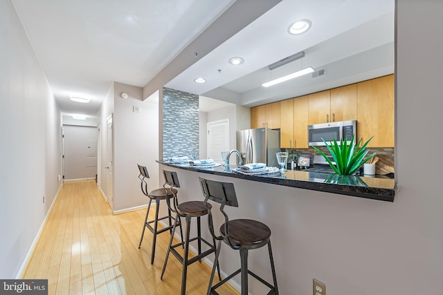 kitchen with stainless steel appliances, a kitchen breakfast bar, kitchen peninsula, and light hardwood / wood-style floors