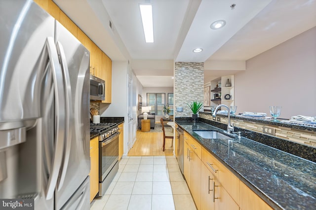 kitchen featuring sink, dark stone countertops, backsplash, light tile patterned floors, and stainless steel appliances