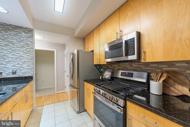 kitchen with dark stone countertops, light tile patterned floors, decorative backsplash, and stainless steel appliances