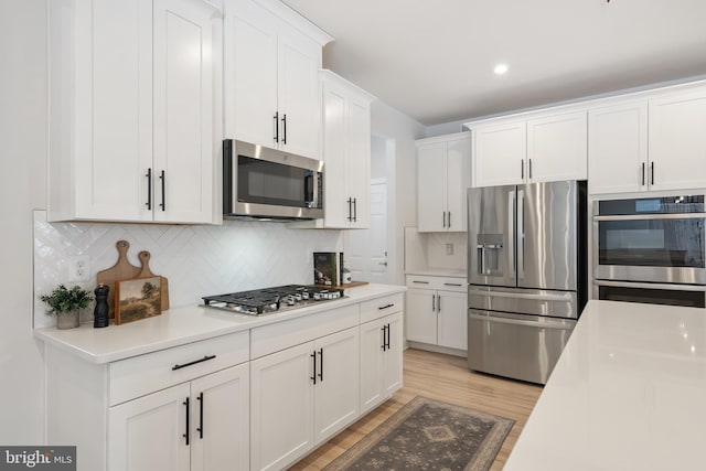 kitchen featuring white cabinetry, backsplash, stainless steel appliances, and light hardwood / wood-style floors