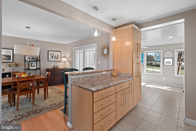 kitchen featuring stone countertops, light brown cabinetry, decorative light fixtures, light tile patterned floors, and kitchen peninsula