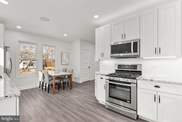 kitchen featuring white cabinetry, light stone counters, light hardwood / wood-style flooring, and appliances with stainless steel finishes