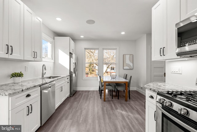 kitchen with white cabinetry, sink, light hardwood / wood-style floors, stainless steel appliances, and light stone countertops