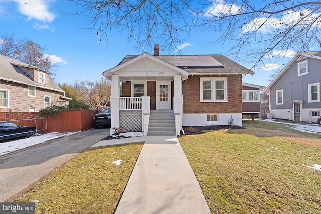 bungalow-style home featuring a porch, a front lawn, and solar panels