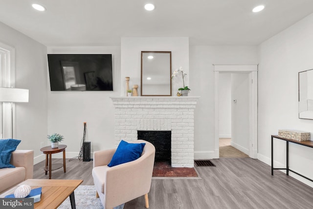 living room featuring a brick fireplace and light wood-type flooring