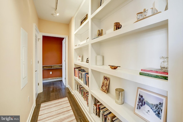 corridor with a baseboard heating unit, track lighting, wood finished floors, and built in features