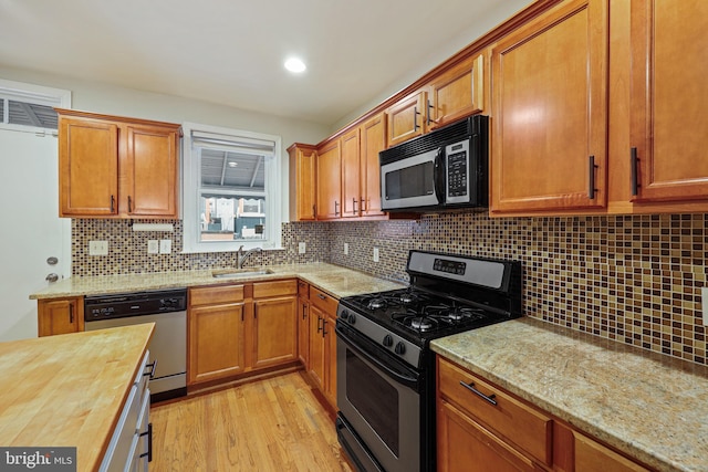 kitchen featuring wood counters, sink, tasteful backsplash, light wood-type flooring, and stainless steel appliances