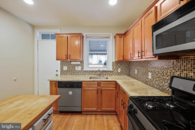 kitchen with sink, light hardwood / wood-style flooring, appliances with stainless steel finishes, backsplash, and light stone counters