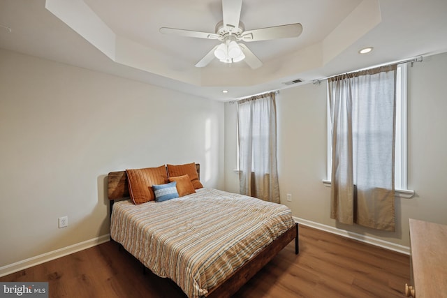 bedroom with dark hardwood / wood-style floors, ceiling fan, and a tray ceiling