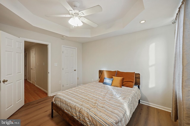 bedroom with a raised ceiling, hardwood / wood-style floors, and ceiling fan