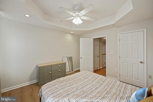 bedroom featuring a raised ceiling, ceiling fan, and light wood-type flooring