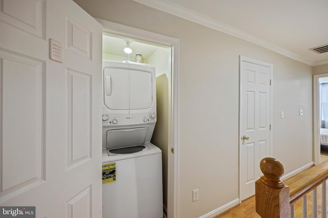 washroom featuring crown molding, stacked washer and clothes dryer, and light wood-type flooring