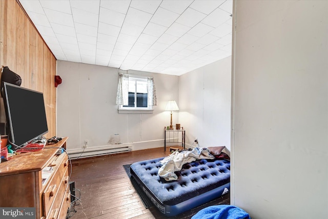 bedroom featuring dark wood-type flooring, wood walls, and a baseboard heating unit