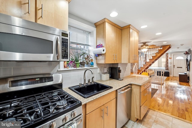 kitchen with light stone counters, stainless steel appliances, light brown cabinetry, and sink